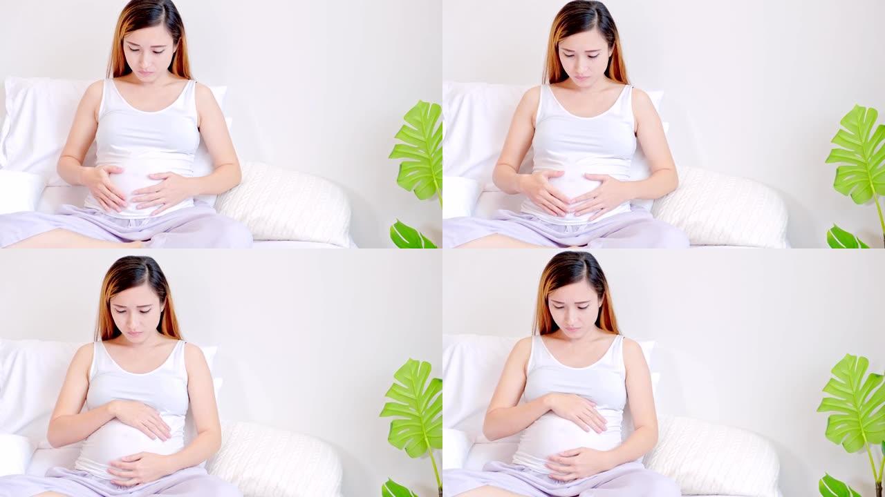 孕妇在床上抚摸着自己的肚子，担心心情。亚洲的女人。年轻父母的概念。