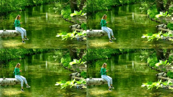 用智能手机在森林河上的原木上的年轻女子