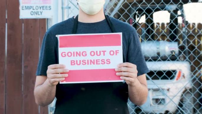 年轻的仓库工人举着 “停业” 的牌子，戴着口罩在他的工作场所关闭的入口