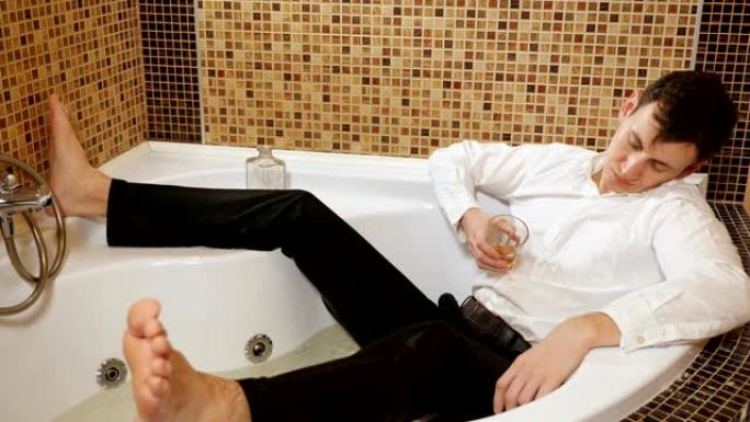 英俊的男人躺在浴缸里喝酒