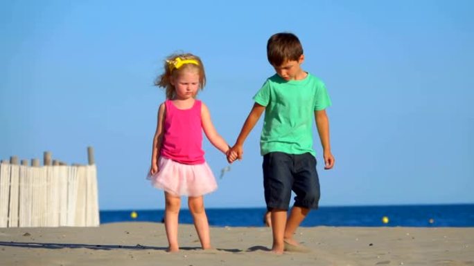 穿着粉红色裙子的小男孩和女孩站在沙滩上扔沙子
