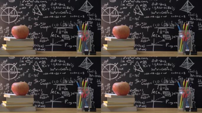 教育背景概念。文具在玻璃罐彩色铅笔，圆规工具，剪刀，直尺，黑板上苹果在书籍和数学公式背景。