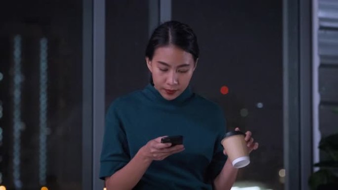 亚洲ux/ui设计师在工作了一整夜后喝咖啡休息时使用移动检查社交媒体来处理modern office