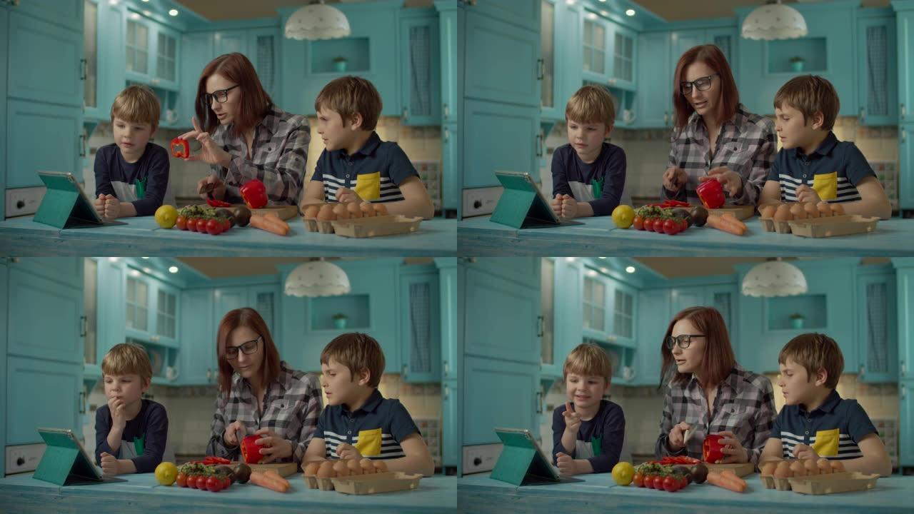 一家人一起烹饪站在蓝色厨房的平板电脑上看在线食谱。两个孩子在家帮妈妈做饭。女人切甜红辣椒。