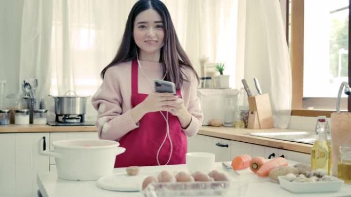 年轻的亚洲妇女用手机听音乐，在厨房跳舞。