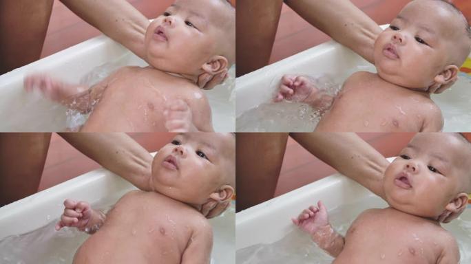 一位亚洲母亲在白色塑料儿童浴缸的浴室里为男婴洗澡的照片