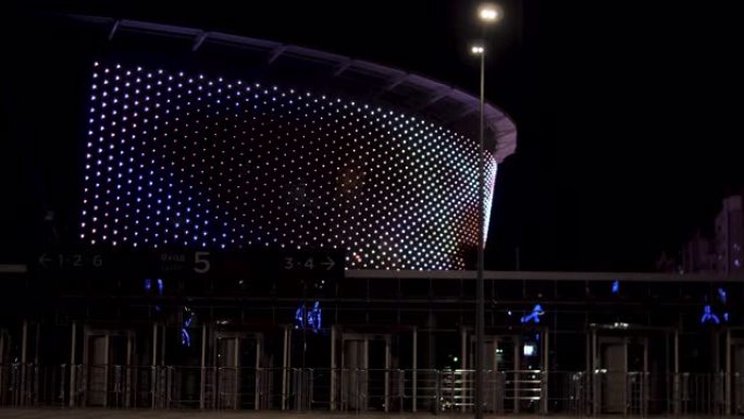 多功能体育场，夜空背景上有许多美丽的灯光。库存镜头。带明亮照明和主入口大门的现代中央足球场