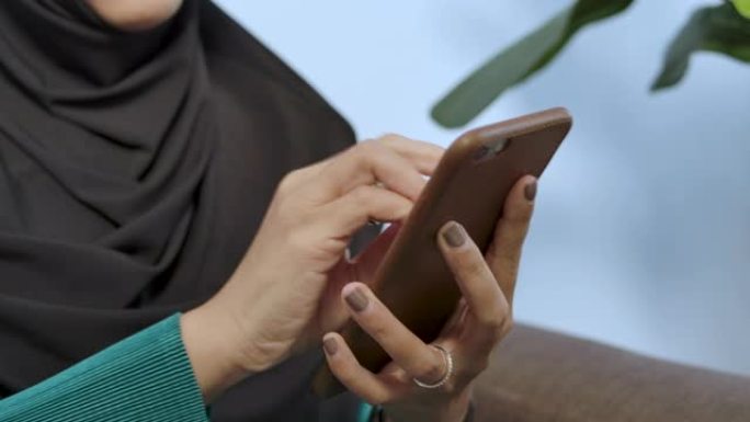 一名年轻穆斯林妇女使用喷雾酒精清洁智能手机的手照-冠状病毒covid 19保护意识概念多样性