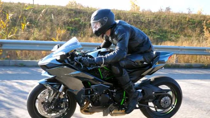 戴着头盔的年轻人骑着现代运动摩托车。摩托车手在乡间小路上骑摩托车。旅途中开车的人。自由和冒险的概念。