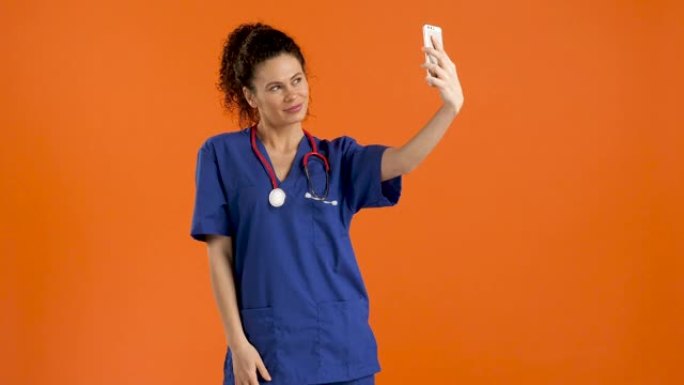 年轻女医生用智能手机自拍，橙色背景