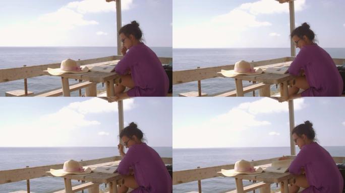 在阳光明媚的日子里，年轻女子坐在海边帕尔马罗拉岛的木制阳台上看书。白色裙子和帽子的紫色连衣裙。