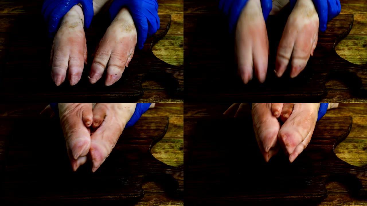 戴着橡胶手套的人的手在木制厨房板上用猪蹄滑稽地敲打。