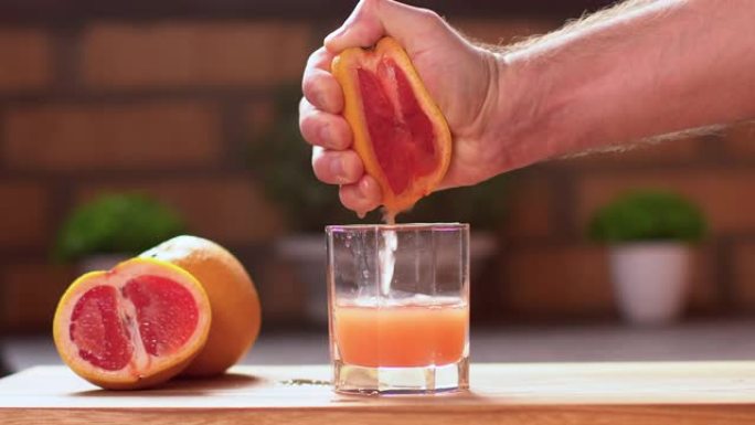 无法辨认的人挤压一半成熟多汁的葡萄柚的特写镜头。新鲜柑橘汁下降。