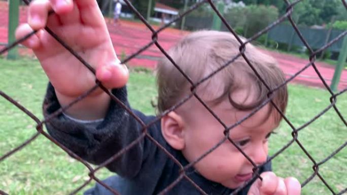 可爱的宝宝抱着游戏栅栏从外面看