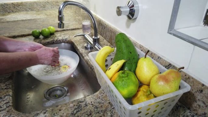 手的特写，在家用厨房水槽中洗涤水果 (苹果)