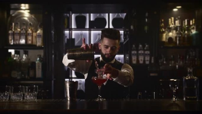 调酒师正在将调酒器中的酒精通过鸡尾酒过滤器倒入玻璃杯中。4k