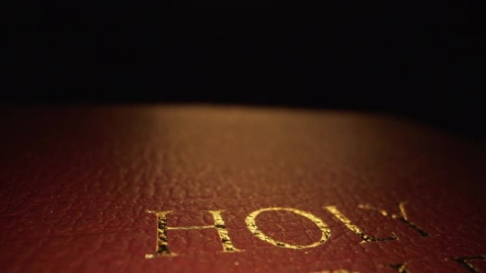 极端微距特写移动滑块揭示拍摄的黄金文字标题“圣经”封面纹理图案书上帝的话在一个黑暗的背景与独特的照明