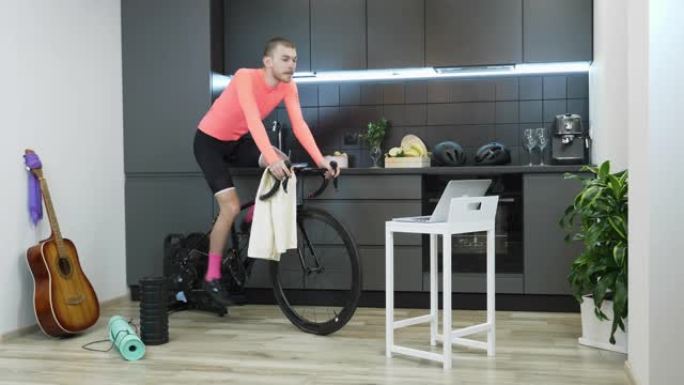 在冠状病毒大流行期间，运动男子在家接受自行车固定教练的训练，以实现社交距离自我隔离的检疫。穿着粉色运
