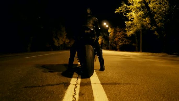 戴着头盔和皮夹克的骑自行车的人在夜间高速公路上坐在摩托车上，准备骑车。男人打算在晚上骑摩托车。自由和
