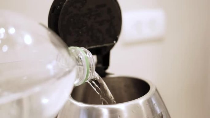 一个人的手将水从瓶子倒入厨房的电热水壶的特写镜头。