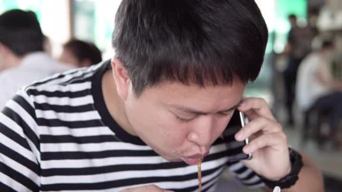 亚洲男子在使用智能手机时吃面。