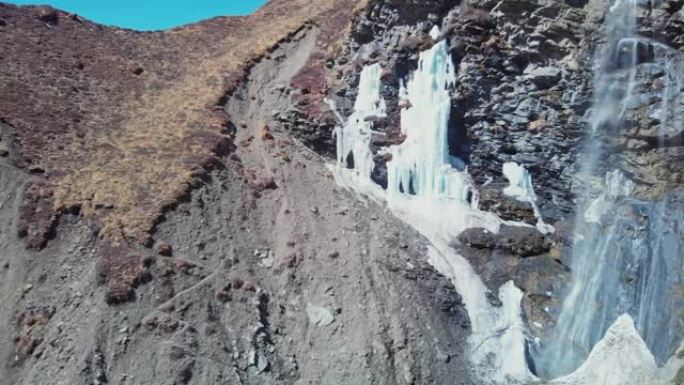 令人惊叹的山瀑布从岩石卵石悬崖上落下，冰柱结冰