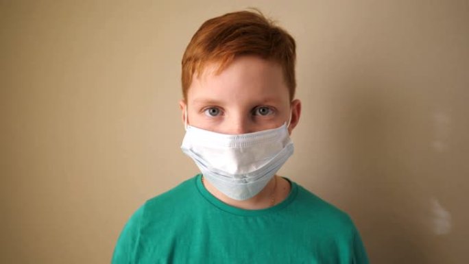 戴着医用口罩看着相机的小男孩的肖像。悲伤的男孩子戴着防护面具从病毒里面。冠状病毒和流行病的健康和安全