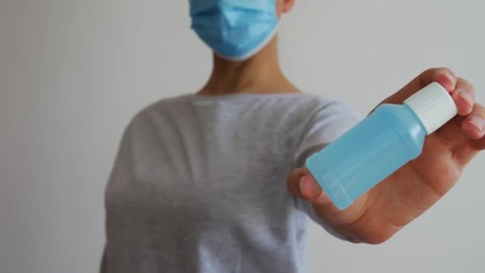 一个戴着蓝色医用口罩的女人手里的酒精凝胶。