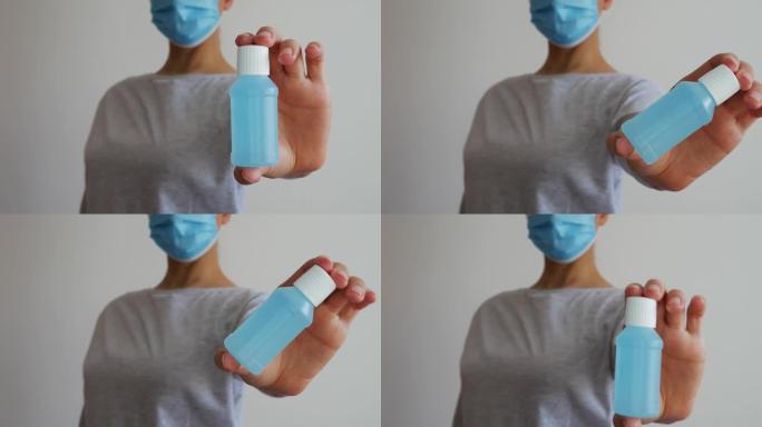 一个戴着蓝色医用口罩的女人手里的酒精凝胶。