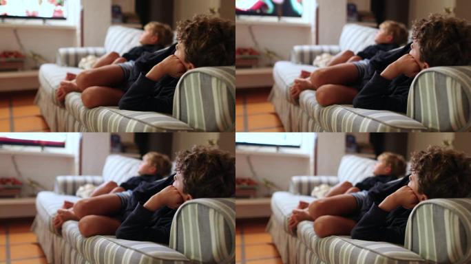 孩子们晚上看电影。两个兄弟躺在沙发上盯着屏幕看电影