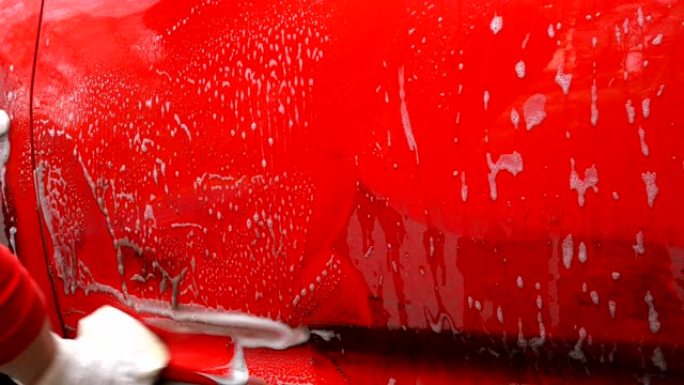 穿红色衣服的女人用海绵和肥皂泡沫手洗肮脏的红色汽车。