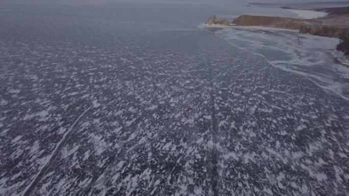 日落时分，俄罗斯西伯利亚奥尔洪岛胡日尔，在冰冻的贝加尔湖上行驶的汽车航拍画面。沙曼卡山布尔汉角。美丽