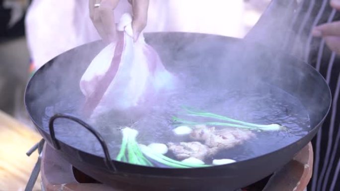 大厨正在将巨大的未煮熟的五花肉浸入沸水中。