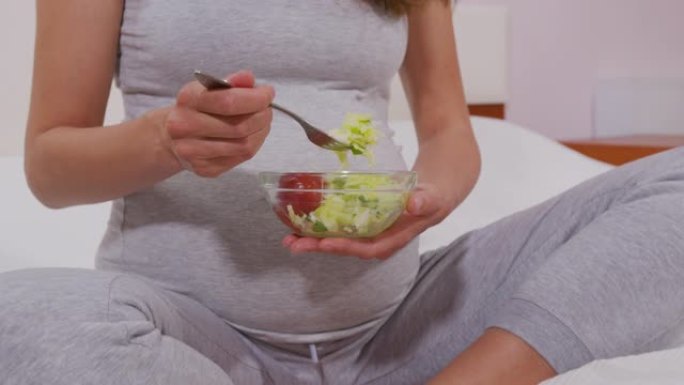 一个孕妇用叉子吃蔬菜沙拉，适当的营养。孕妇吃了对未出生的孩子有用的蔬菜沙拉。正确的营养概念。