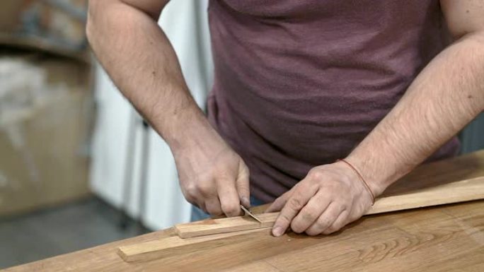 男人的手用小刀切开一块木板。