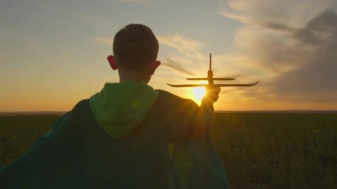 一个男孩手里拿着一架飞机跑过田野。日落。4K