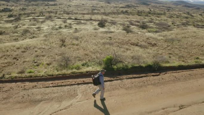 一个徒步旅行者在干燥丘陵的风景中独自沿着一条土路行走。