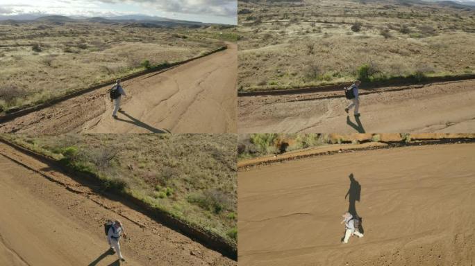 一个徒步旅行者在干燥丘陵的风景中独自沿着一条土路行走。