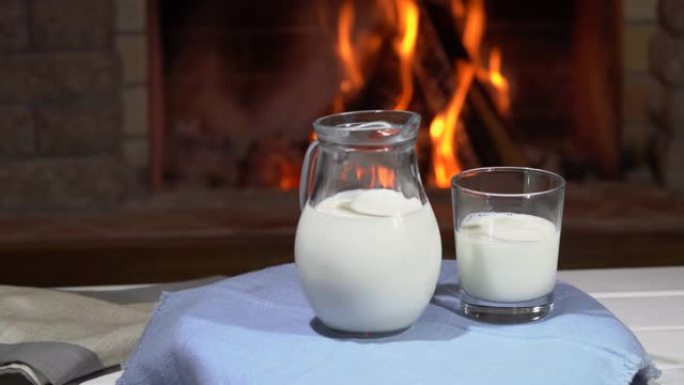 带玻璃壶和带牛奶的玻璃的桌子在舒适的壁炉前旋转，在乡村别墅中，寒假。