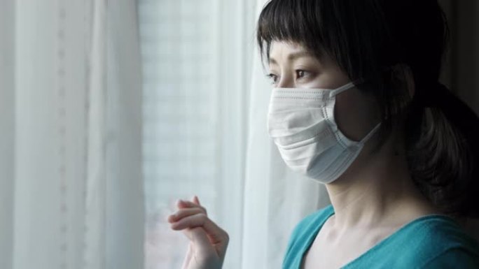 戴着外科口罩的亚洲妇女的室内肖像向窗外看