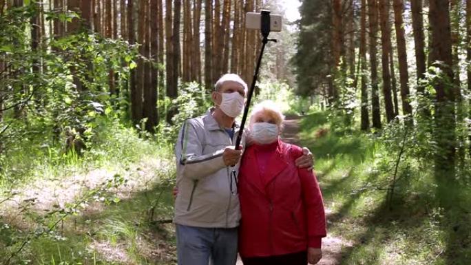 一对戴着防护口罩的老年夫妇在智能手机上自拍并在公园散步，检疫后在新鲜空气中散步，这是针对病毒的预防措