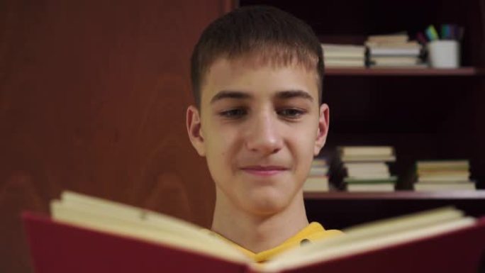 年轻的学生正在看书，在家庭办公室里一个装有教科书和学习用品的木制书柜的背景上大笑。穿着黄色运动衫