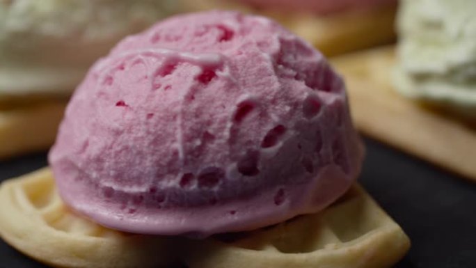 自制华夫饼的特写镜头，彩色冰ream顶部旋转。慢动作在华夫饼上的粉红色和绿色开心果冰ream球。