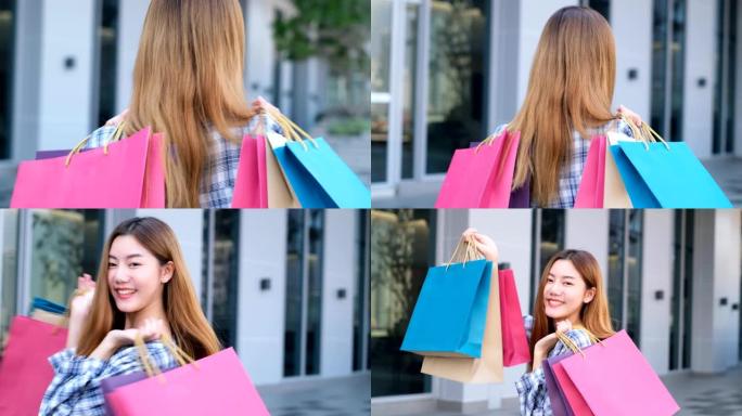 微笑的年轻亚洲女人，购物中心背景上的彩色包。使用智能手机在线购物，站在商场大楼时微笑。生活方式概念