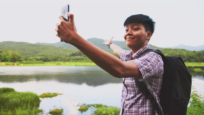 微笑的亚洲男子使用手机连接互联网手机与河流和青山景观给女朋友。人们徒步旅行背包的概念。