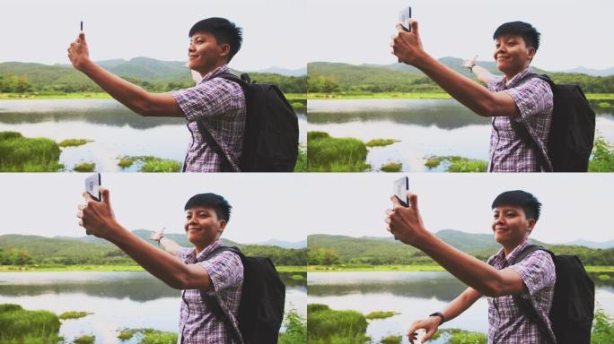微笑的亚洲男子使用手机连接互联网手机与河流和青山景观给女朋友。人们徒步旅行背包的概念。