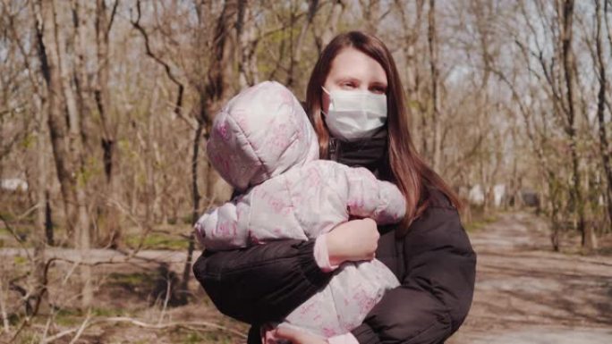 戴着防护面具的妈妈带着婴儿在公园散步。冠状病毒大流行条件。带着孩子的女人的严肃表情