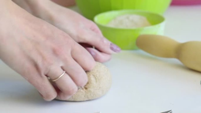 一个女人用手揉捏一块生面团做新鲜蛋糕。桌子表面附近有擀面杖和面粉。准备无酵饼。特写。