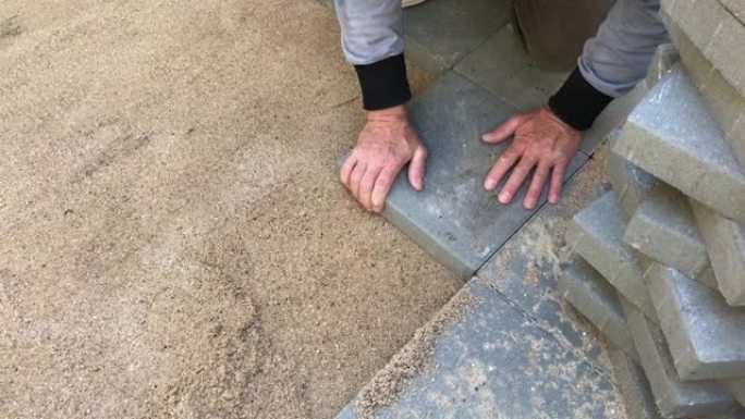 铺路工铺设成排的混凝土方形摊铺机或瓷砖，很好地铺设在准备好的平坦沙面上。快速运动视频剪辑。