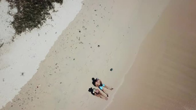 一对夫妇躺在印度尼西亚龙目岛粉红海滩海滨的沙滩上玩无人机。波浪轻轻地冲刷着海岸。他们在晒黑。快乐和粗